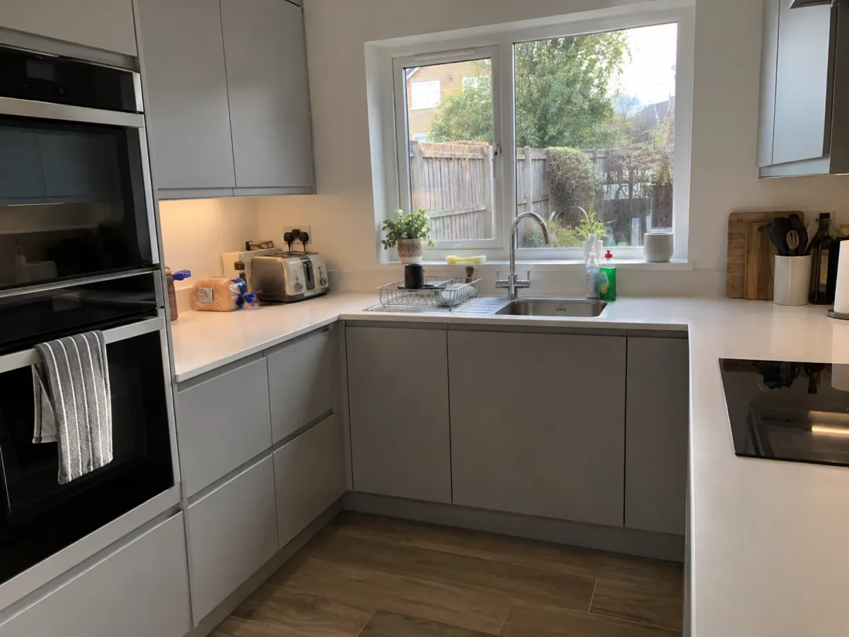 Light grey handleless kitchen with integrated double oven under a window